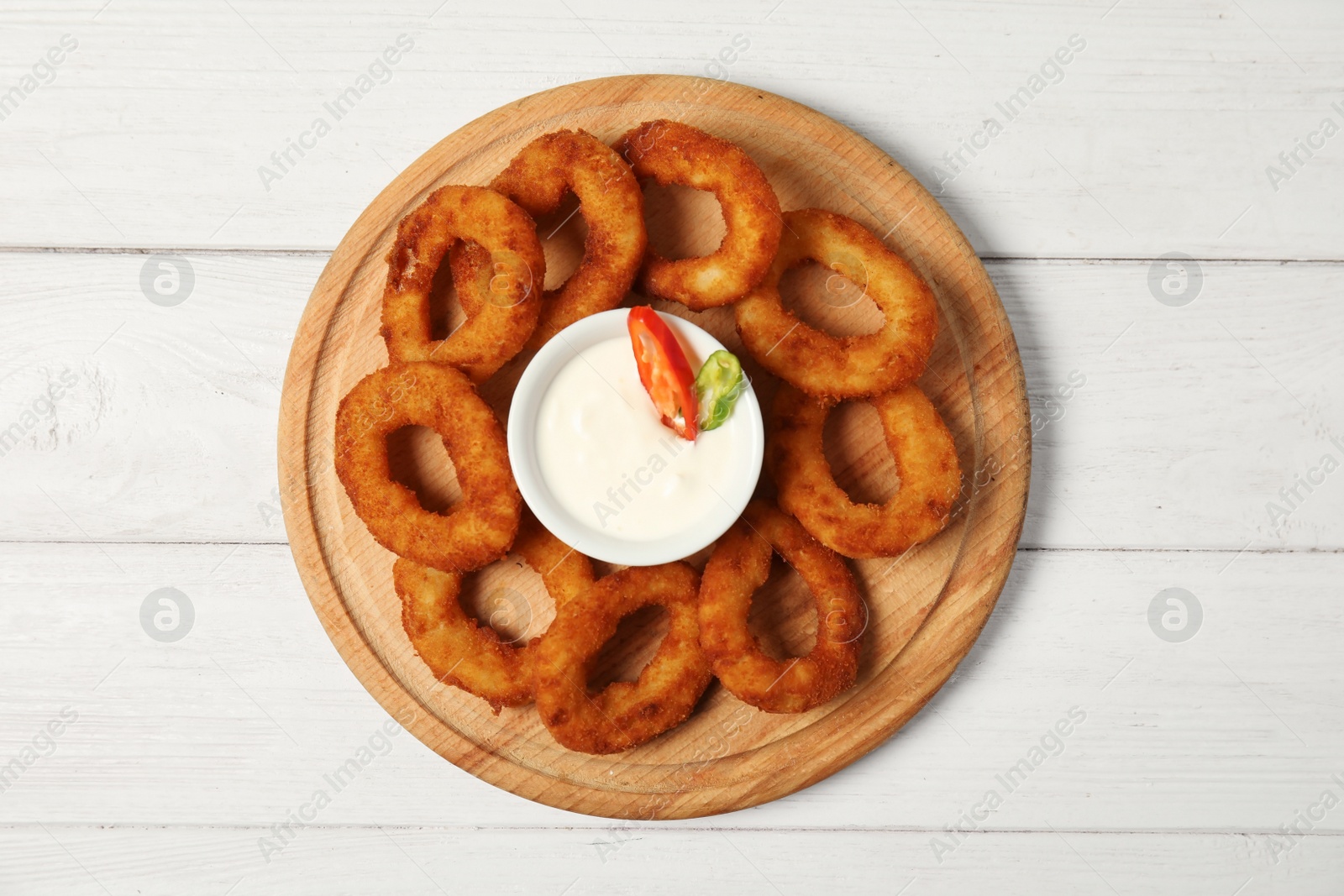 Photo of Wooden board with tasty onion rings and sauce on table, top view