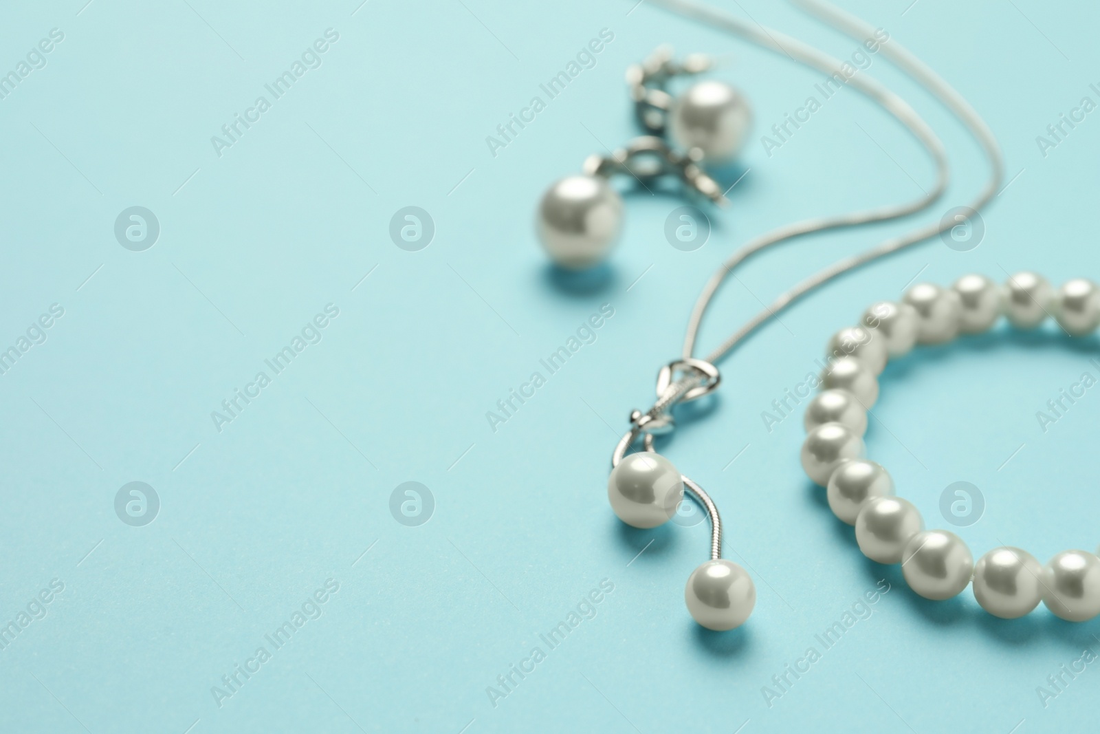 Photo of Elegant necklace, bracelet and earrings with pearls on light blue background, closeup. Space for text