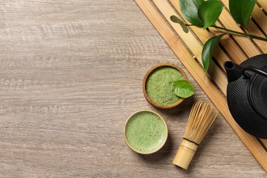 Photo of Cup of fresh matcha tea, bamboo whisk, teapot and green powder on wooden table, flat lay. Space for text