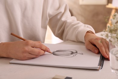 Woman drawing bell pepper with graphite pencil in sketchbook at table, closeup