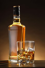 Photo of Whiskey with ice cubes in glass and bottle on wooden table