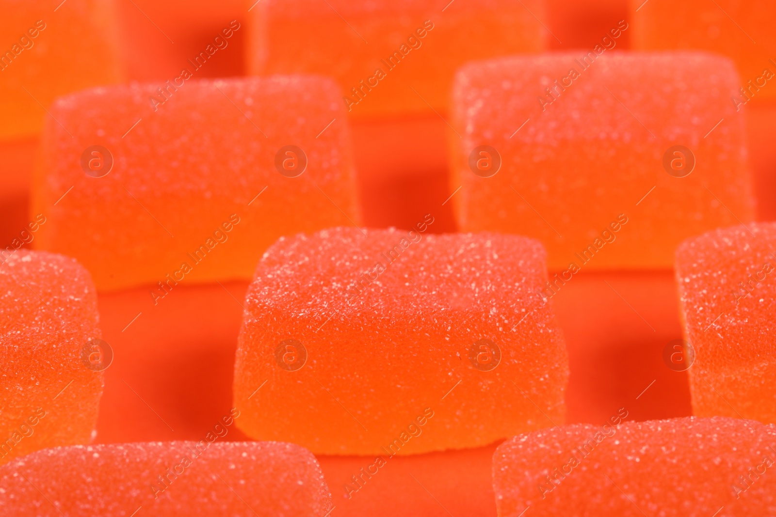 Photo of Tasty orange jelly candies on coral background, closeup
