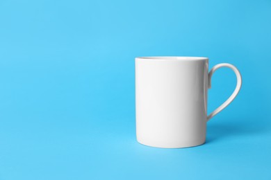 Photo of One white ceramic mug on light blue background. Space for text