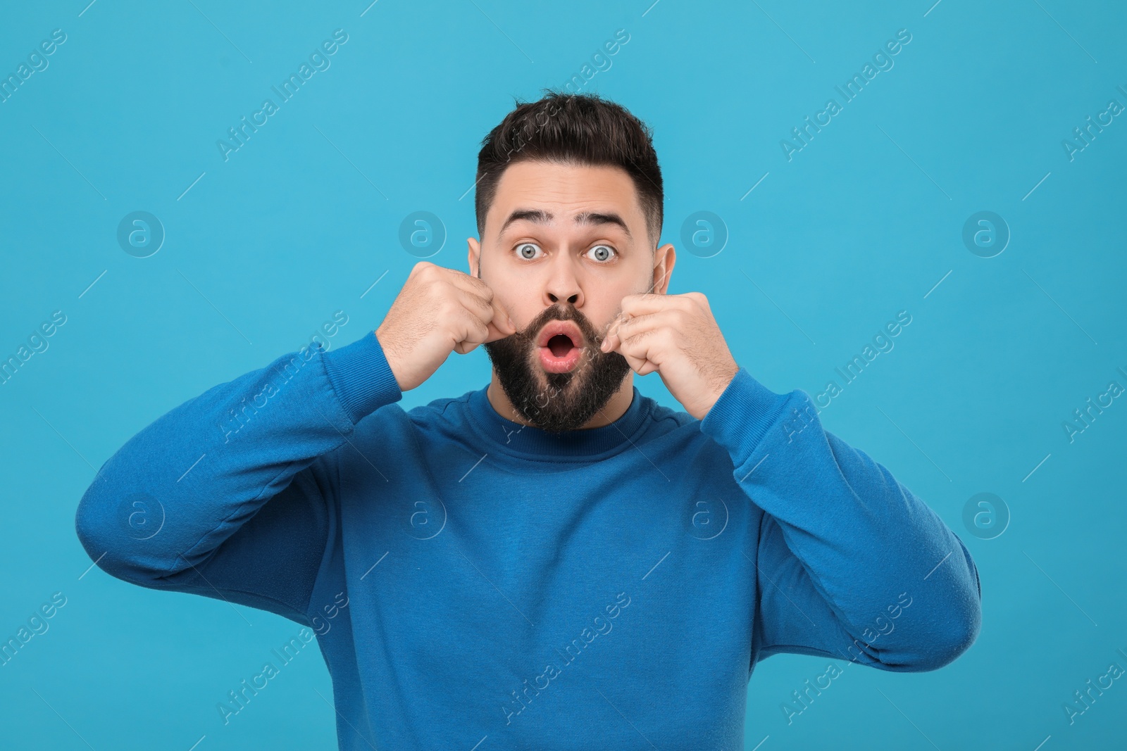 Photo of Surprised young man touching mustache on light blue background