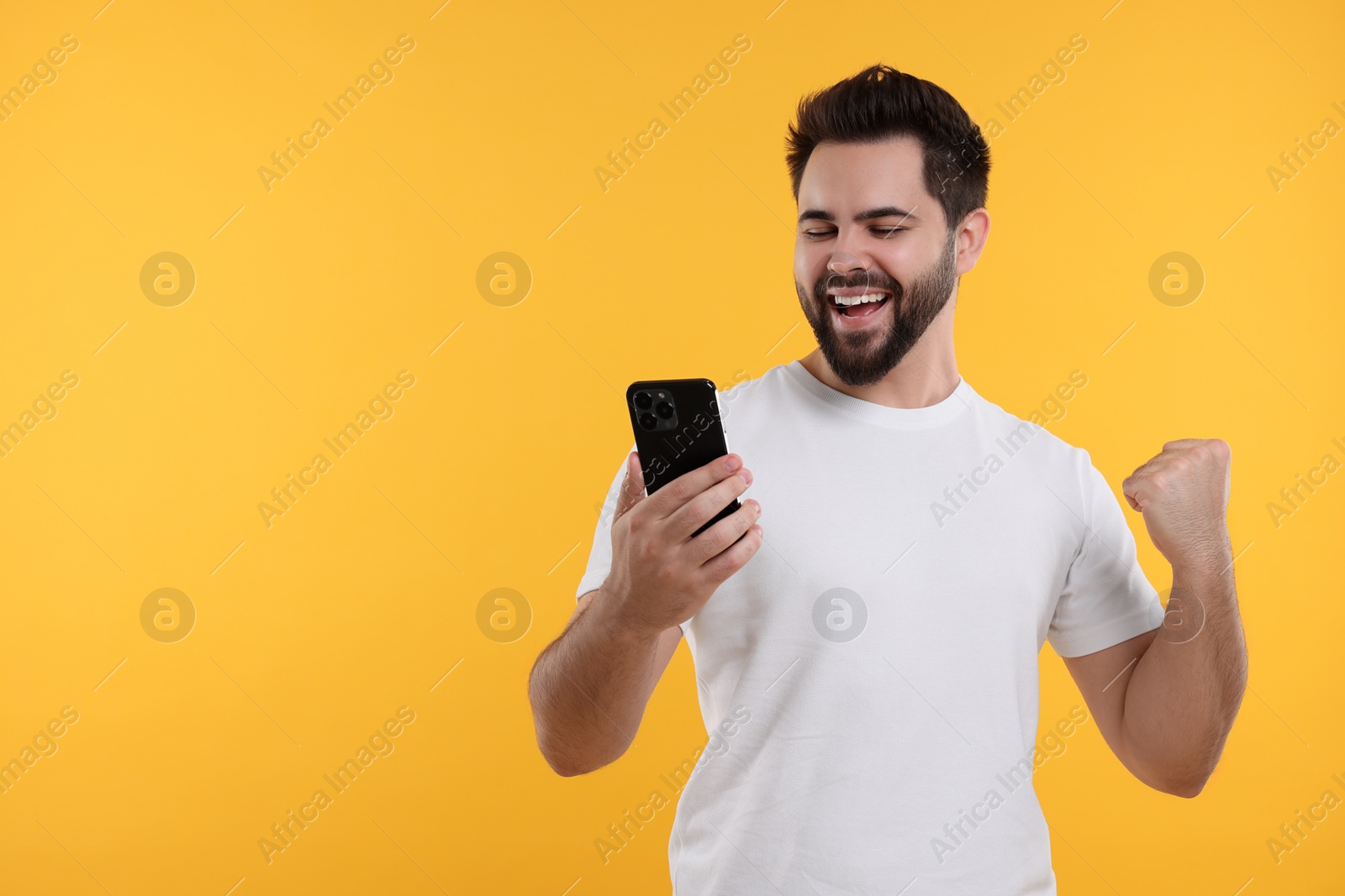 Photo of Happy young man using smartphone on yellow background, space for text