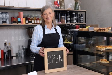 Photo of Happy business owner holding open sign at cashier desk in her cafe