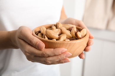 Photo of Woman holding bowl with Brazil nuts on blurred background, closeup