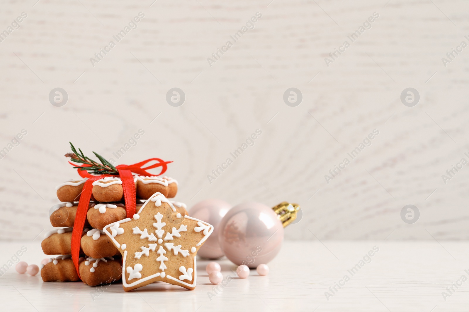 Photo of Tasty Christmas cookies tied with red ribbon near festive decor on beige wooden table, space for text