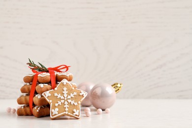 Tasty Christmas cookies tied with red ribbon near festive decor on beige wooden table, space for text