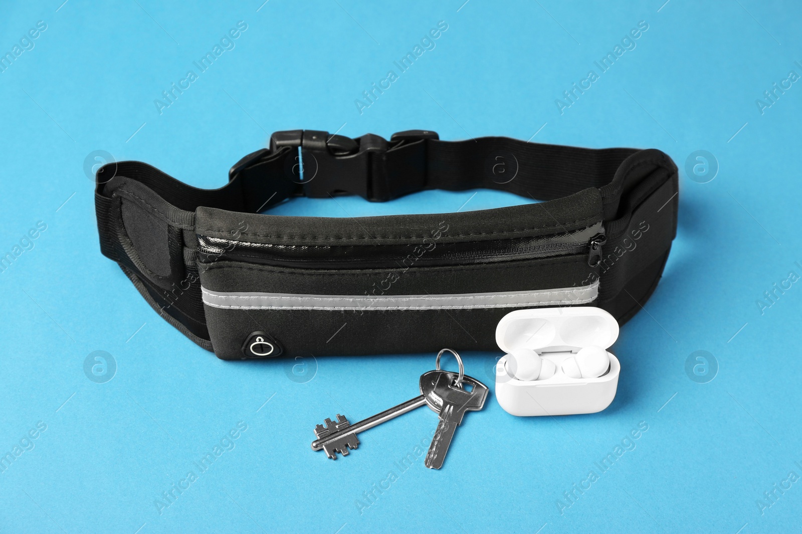 Photo of Stylish black waist bag, keys and earphones on light blue background