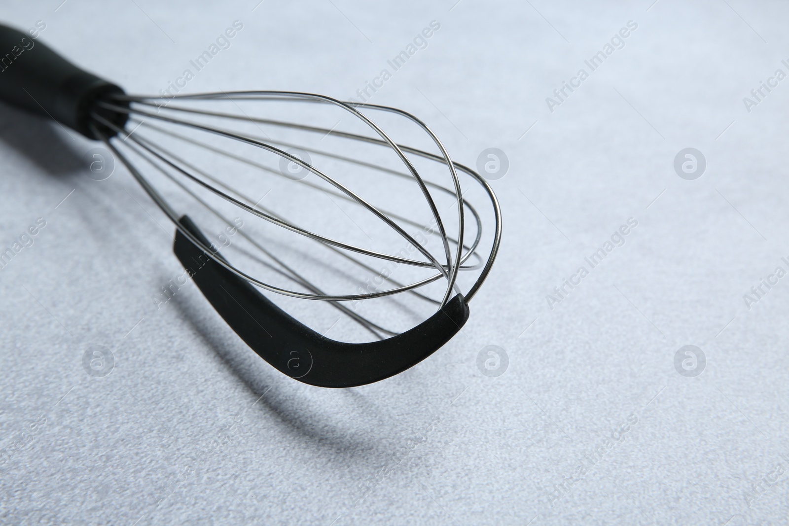 Photo of Metal whisk on gray table, closeup. Space for text