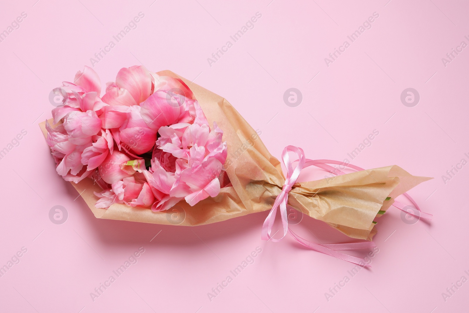 Photo of Beautiful bouquet of peonies wrapped in paper on pink background, top view