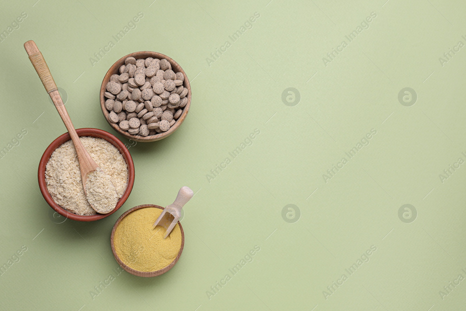 Photo of Beer yeast powder, flakes and pills on light green background, flat lay. Space for text