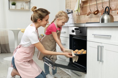 Photo of Mother and her daughter taking out cookies from oven in kitchen