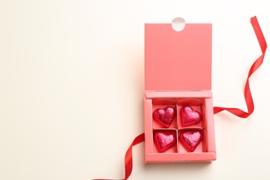 Photo of Heart shaped chocolate candies and ribbon on beige background, flat lay. Space for text