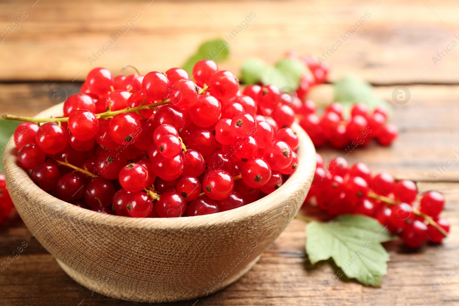 Photo of Ripe red currants in bowl on wooden table, closeup