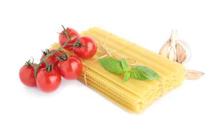 Photo of Uncooked lasagna sheets with cherry tomatoes, garlic and basil isolated on white