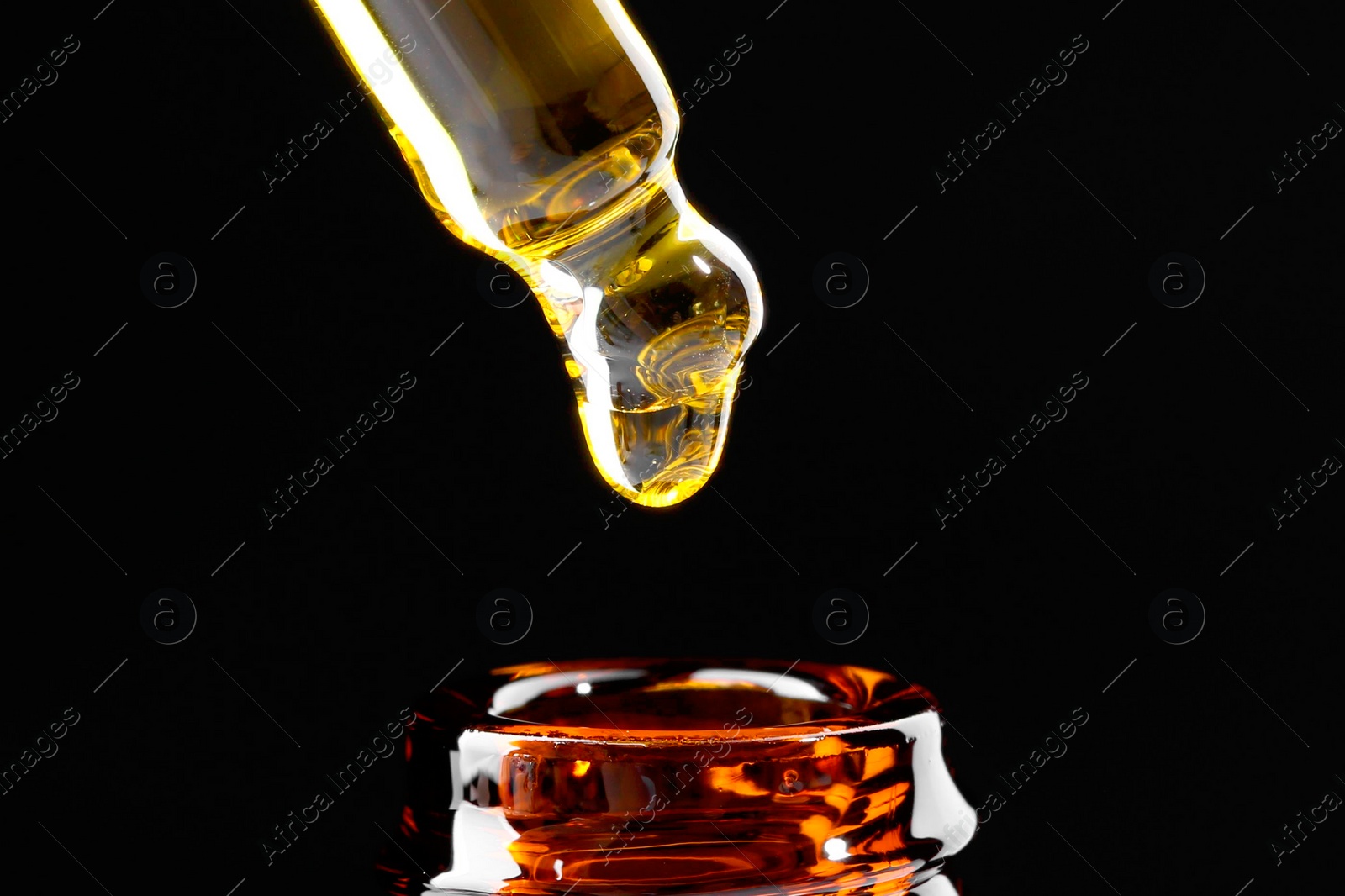 Photo of Dripping tincture from pipette into bottle on black background, closeup