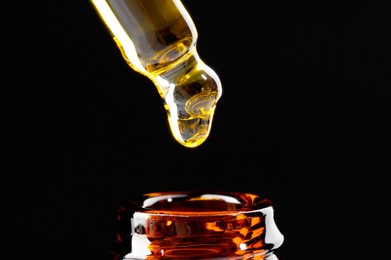 Photo of Dripping tincture from pipette into bottle on black background, closeup