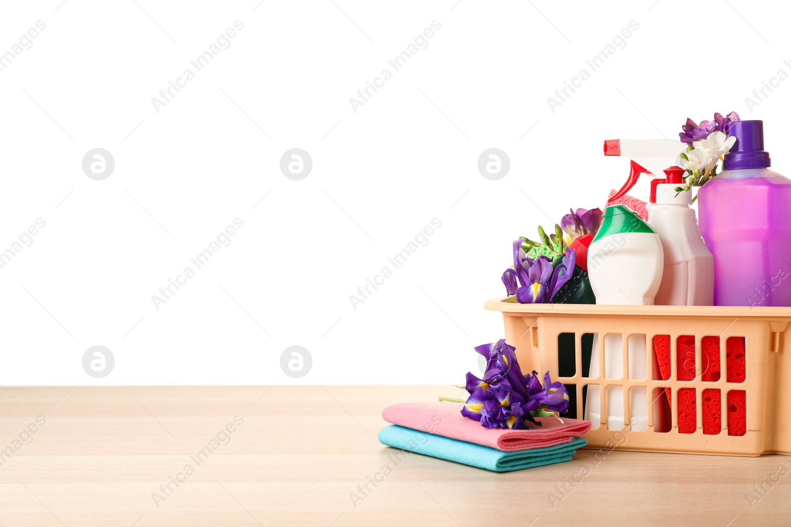 Photo of Plastic basket with spring flowers and cleaning supplies on wooden table. Space for text