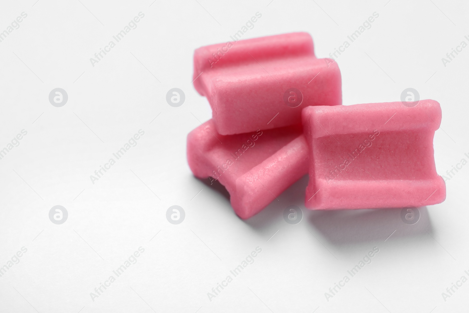 Photo of Tasty pink chewing gums on white background, closeup. Space for text