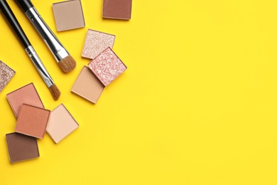 Beautiful eye shadow refill pans and makeup brushes on yellow background, flat lay. Space for text