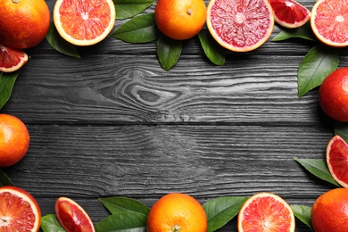 Photo of Frame of whole and cut red oranges on black wooden table, flat lay. Space for text