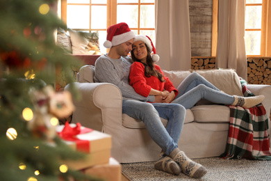 Photo of Happy young couple wearing Santa hats on sofa in living room decorated for Christmas