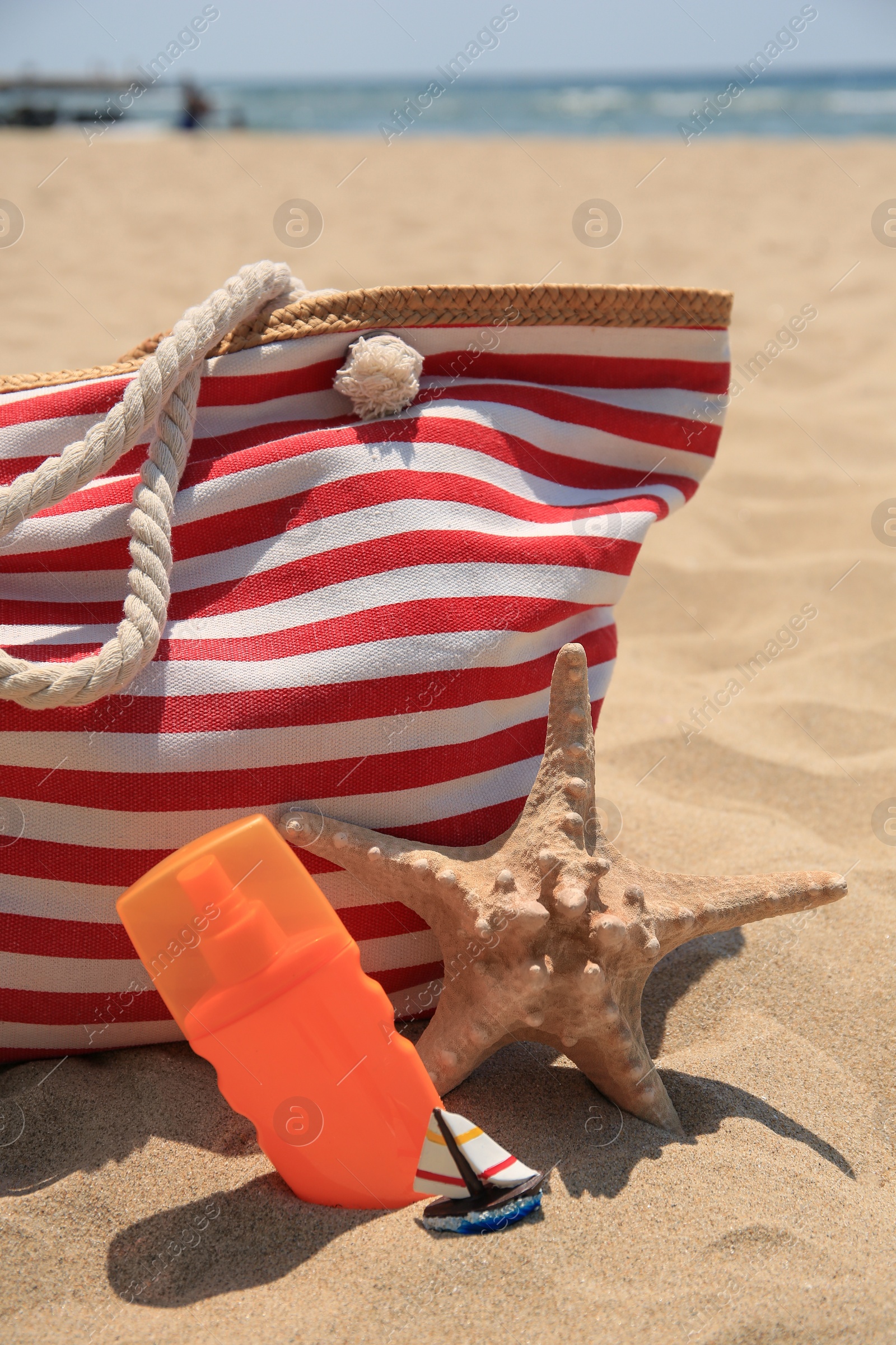 Photo of Bottle of sunscreen, starfish and bag on sand. Sun protection care