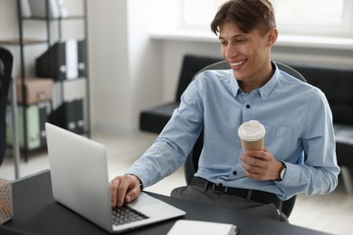 Man with cup of coffee watching webinar at table in office