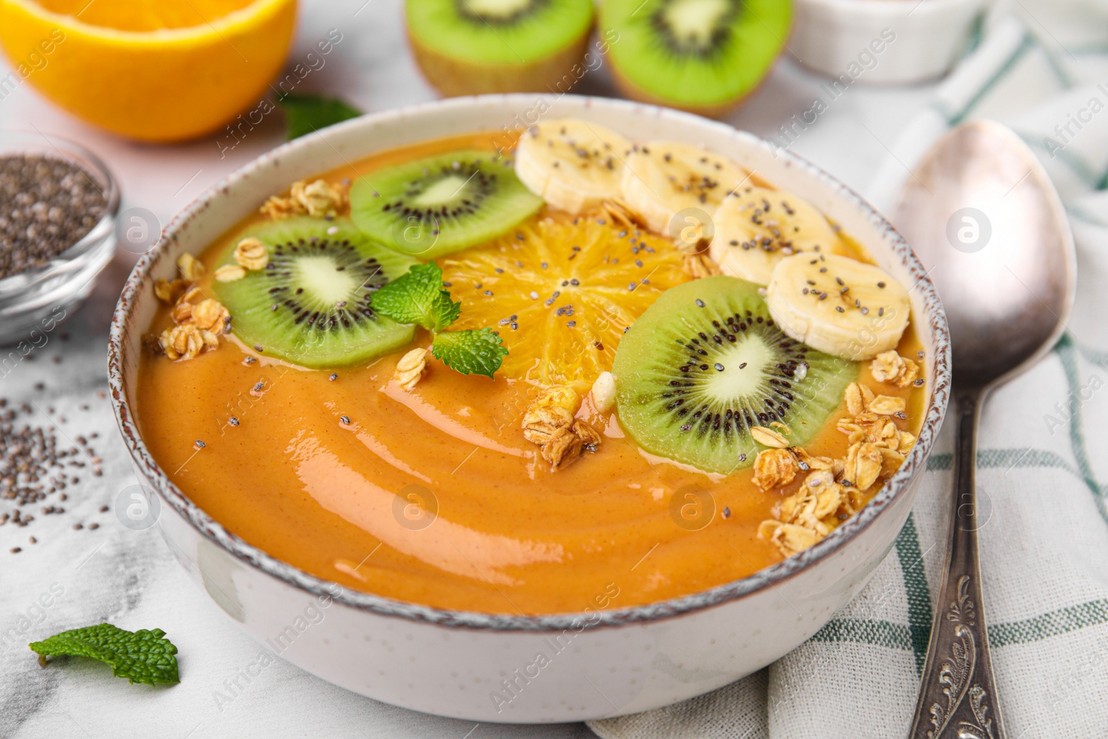 Photo of Bowl of delicious fruit smoothie with fresh banana, kiwi slices and granola served on white marble table, closeup