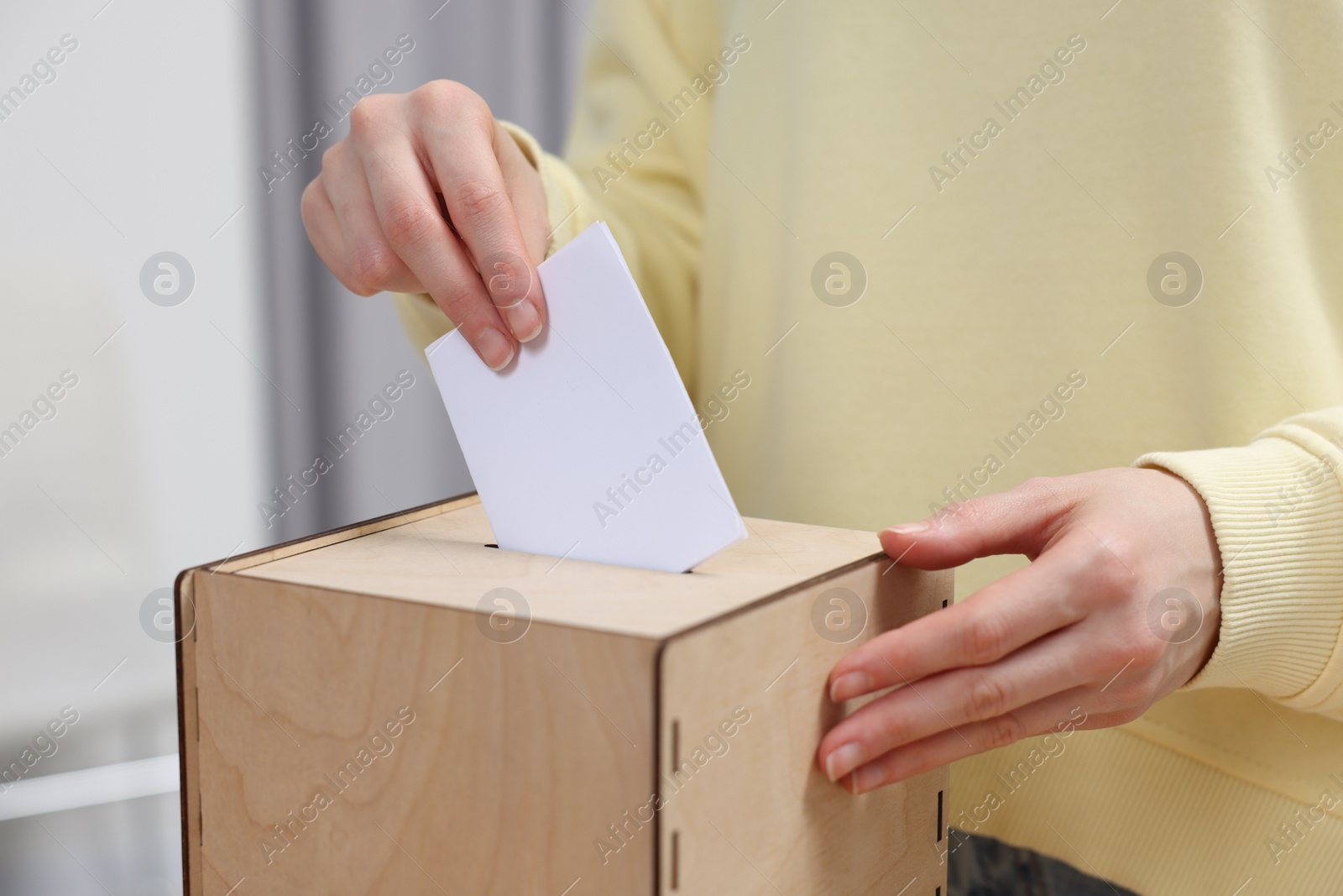 Photo of Woman putting her vote into ballot box on blurred background, closeup