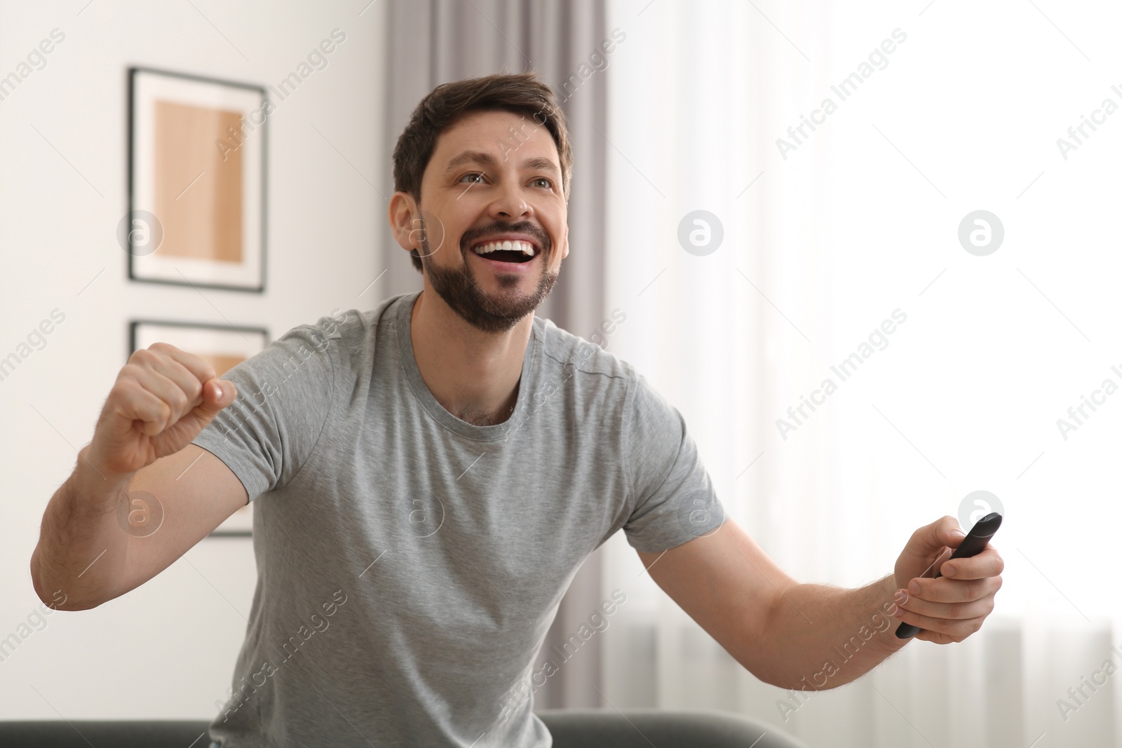 Photo of Emotional man holding remote controller and watching TV at home