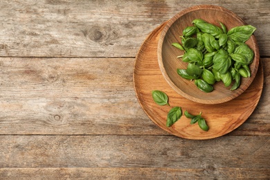 Photo of Bowl with fresh basil on wooden background, top view. Space for text