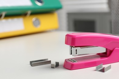 Photo of Stapler and metal staples on white table indoors, space for text