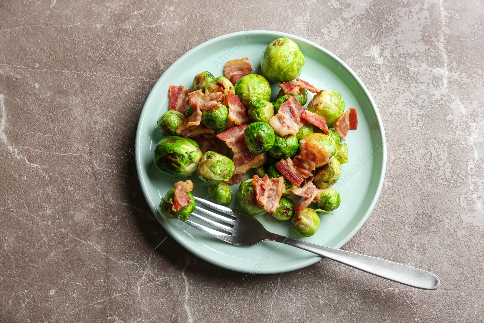 Photo of Delicious Brussels sprouts with bacon on marble table, top view