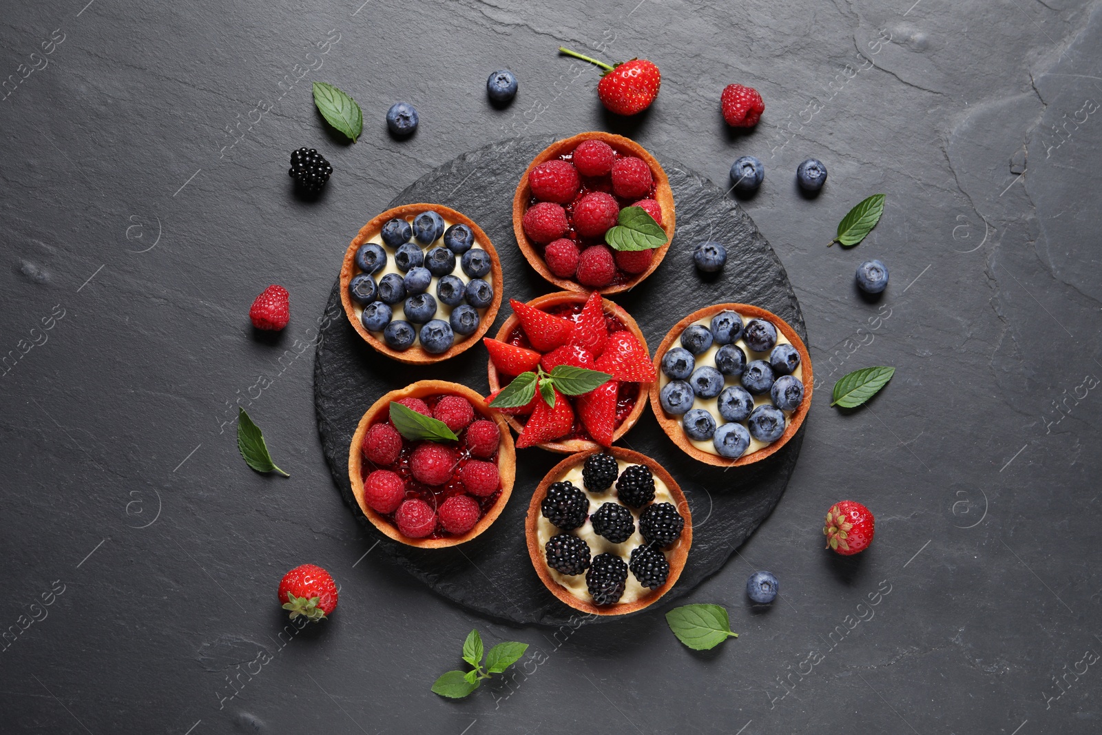 Photo of Tartlets with different fresh berries on black table, flat lay. Delicious dessert