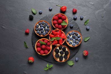 Tartlets with different fresh berries on black table, flat lay. Delicious dessert