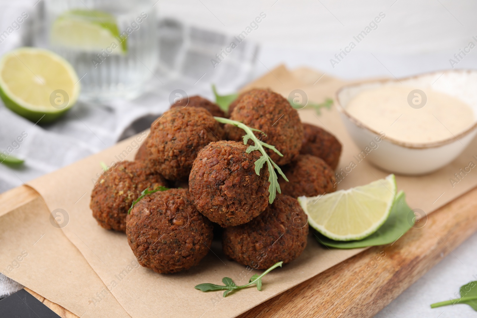 Photo of Delicious falafel balls, arugula, lime and sauce on table