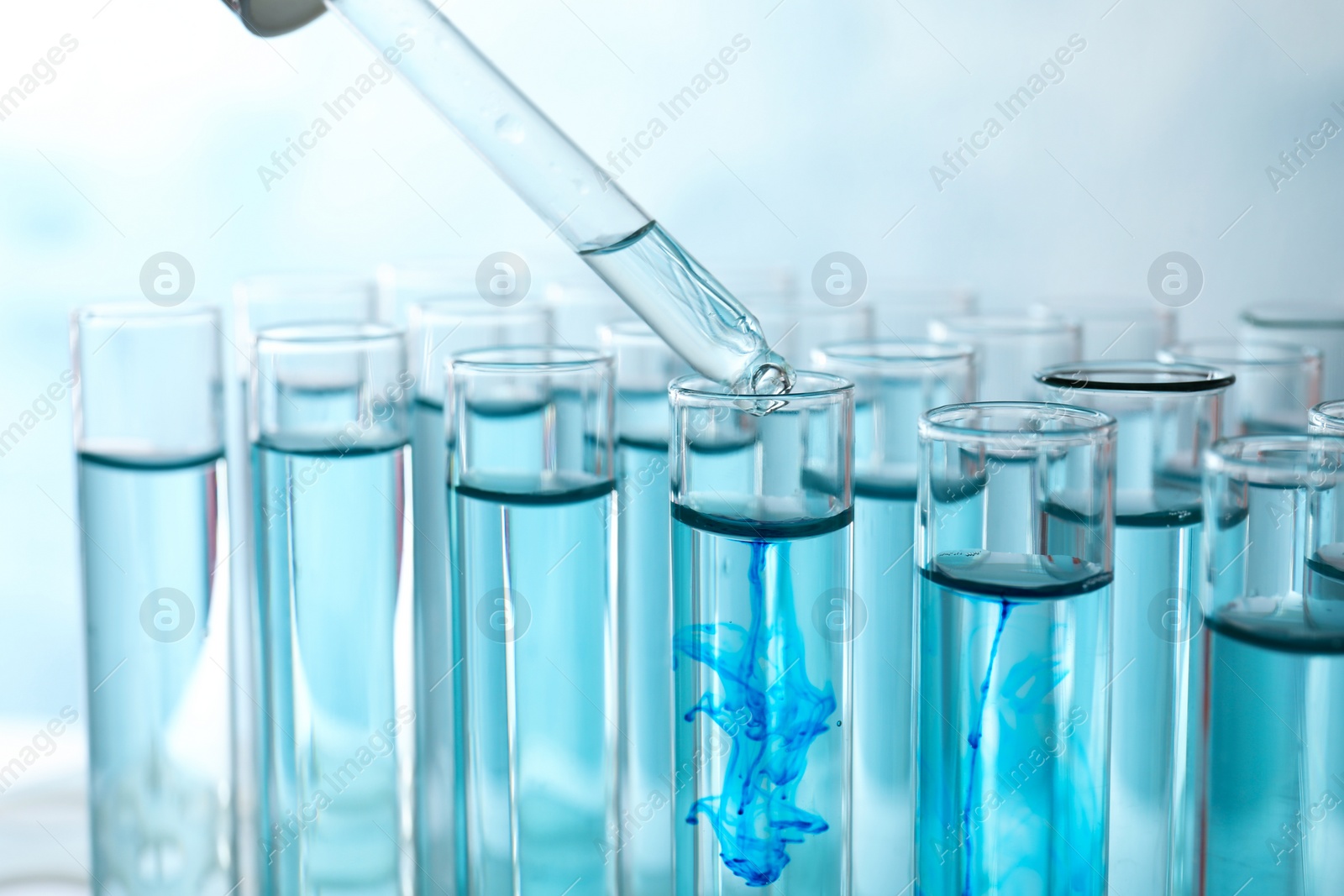 Photo of Dropping sample into test tube with light blue liquid, closeup