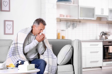 Photo of Man suffering from cough and cold on sofa at home. Space for text