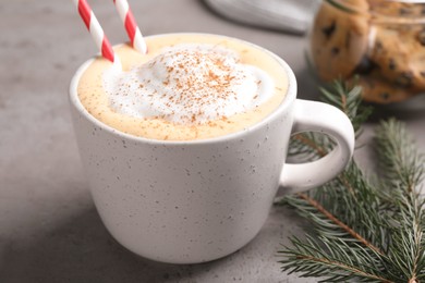 Photo of Cup of delicious eggnog with cinnamon and fir branch on gray table, closeup