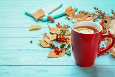 Cup of hot drink and leaves on blue wooden table, space for text. Cozy autumn atmosphere