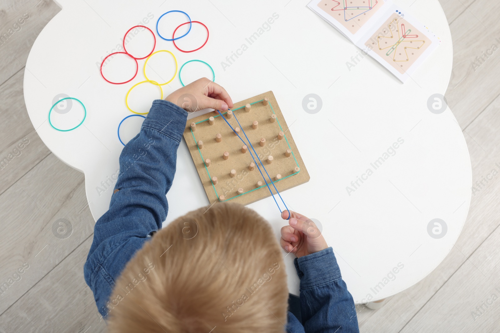 Photo of Motor skills development. Boy playing with geoboard and rubber bands at white table, top view