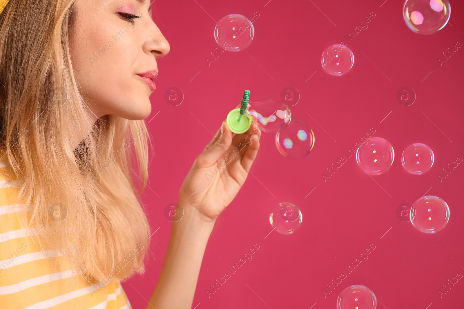 Photo of Young woman blowing soap bubbles on pink background, closeup. Space for text