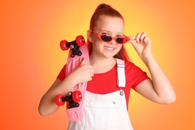 Photo of Cute indie girl with sunglasses and penny board on color background