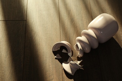 Photo of Broken pink ceramic vase on wooden floor. Space for text