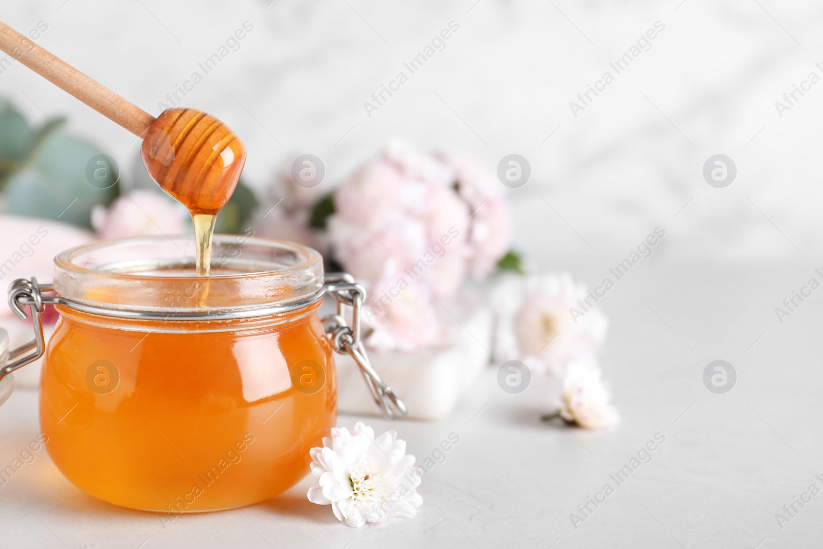 Photo of Jar of organic honey and chrysanthemum flower on light table. Space for text