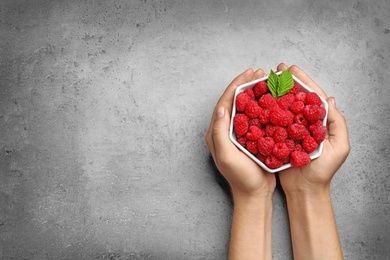 Photo of Woman holding bowl with delicious ripe raspberries on stone background, top view. Space for text