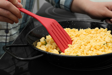 Photo of Woman cooking tasty scrambled eggs in wok pan on stove, closeup